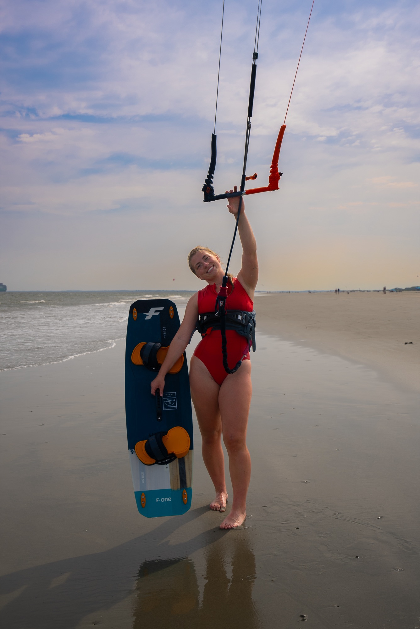 Syd Meyer with her kite bar overhead and her board, on a flat beach