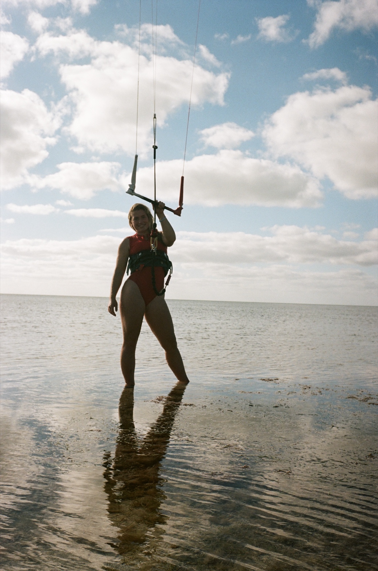 Syd Meyer standing in shallow water with her kite bar overhead, shot on film
